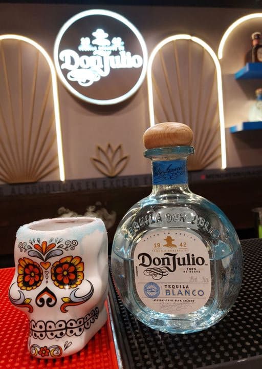 en la imagen se ve la botella de Don Julio Blanco sobre la barra, junto con el vaso del cóctel q es una carabela pintada al estilo mexicano
