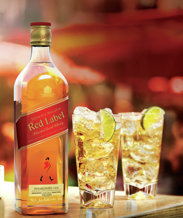 En la imagen se aprecia una botella de whisky Johnnie Walker Red Label junto a dos vasos highball con whisky, hielo y limón.