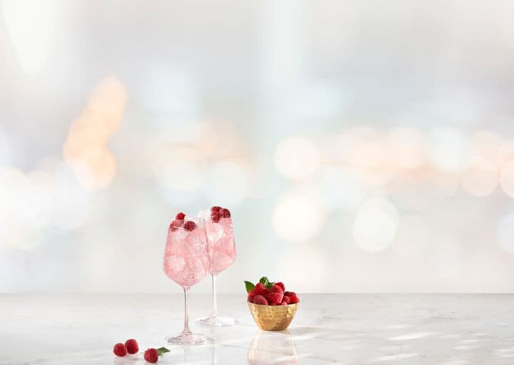 La imagen muestra dos copas con cócteles preparados con vodka Smirnoff Raspberry, junto con un bol con frambuesas.