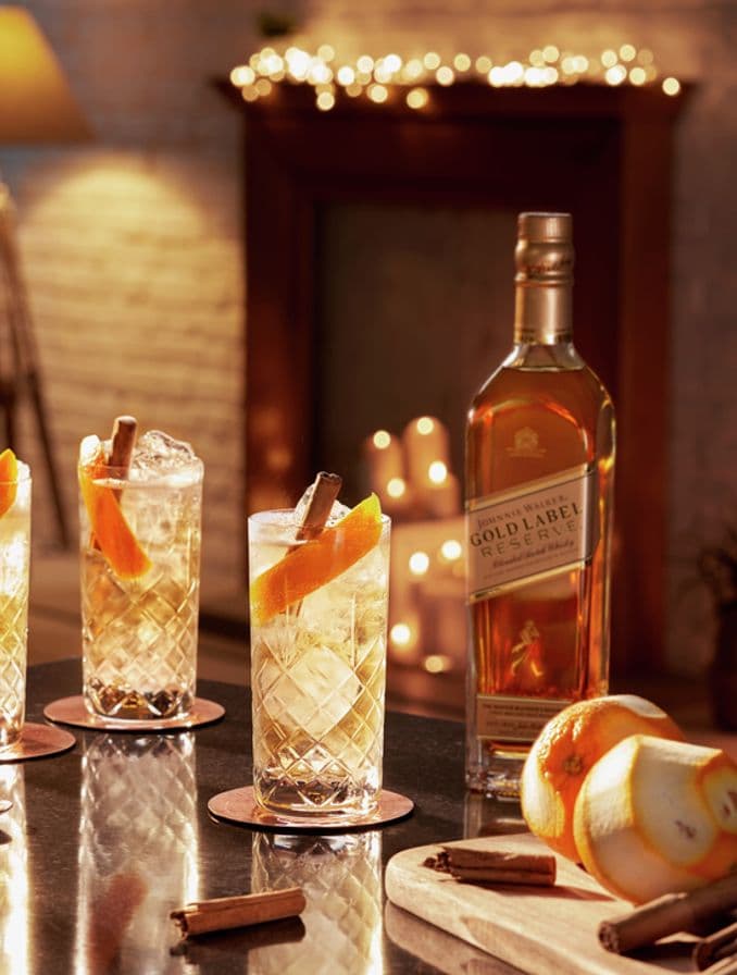 En la imagen se pueden observar tres vasos highball junto a una botella de whisky Johnnie Walker Gold Label Reserve, dispuestos sobre una mesa con elementos de coctelería.