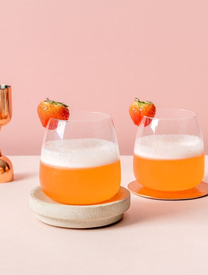 Dos vasos con un cocktail anaranjado y una frutilla como decoración.