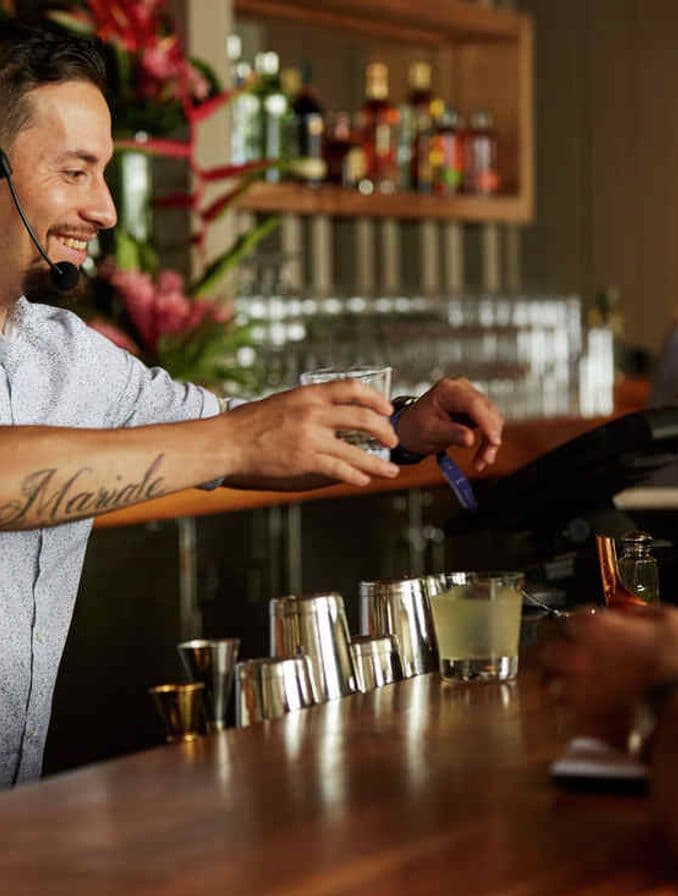 La imagen muestra un bartender sirviendo tragos detrás de una barra.