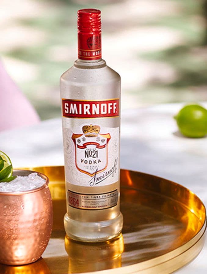 La imagen muestra una botella de vodka Smirnoff N°21 junto a dos vasos de cobre con el cóctel Moscow Mule sobre una bandeja dorada.